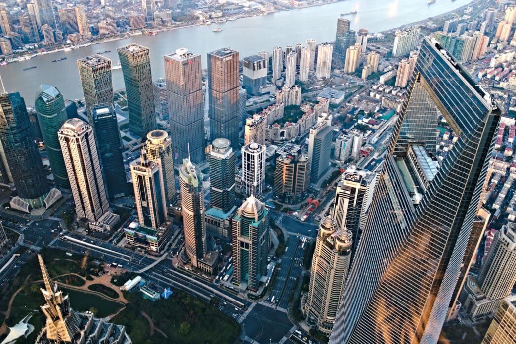 A high aerial view of the Lujiazui financial district in Shanghai, showcasing the Shanghai Tower, the World Financial Center, and the Jin Mao Tower on the Huangpu River's east bank.