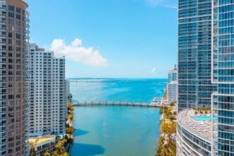 High-angle view of luxury condominium towers flanking a turquoise river leading out to Biscayne Bay with a bridge crossing it.