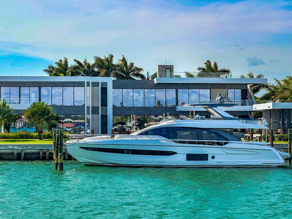 A sleek white yacht is docked in the turquoise water in front of a modern luxury mansion on Miami's Star Island.