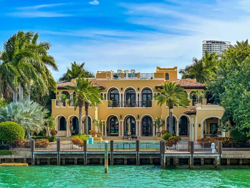 A sprawling, yellow Mediterranean-style luxury mansion on Miami's Star Island, seen from the water with its pool and dock.