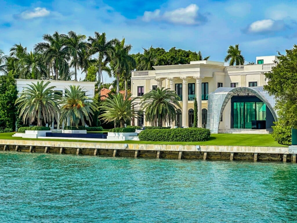 A white neoclassical luxury mansion on Miami's Star Island, featuring a modern glass annex and a waterfront pool.