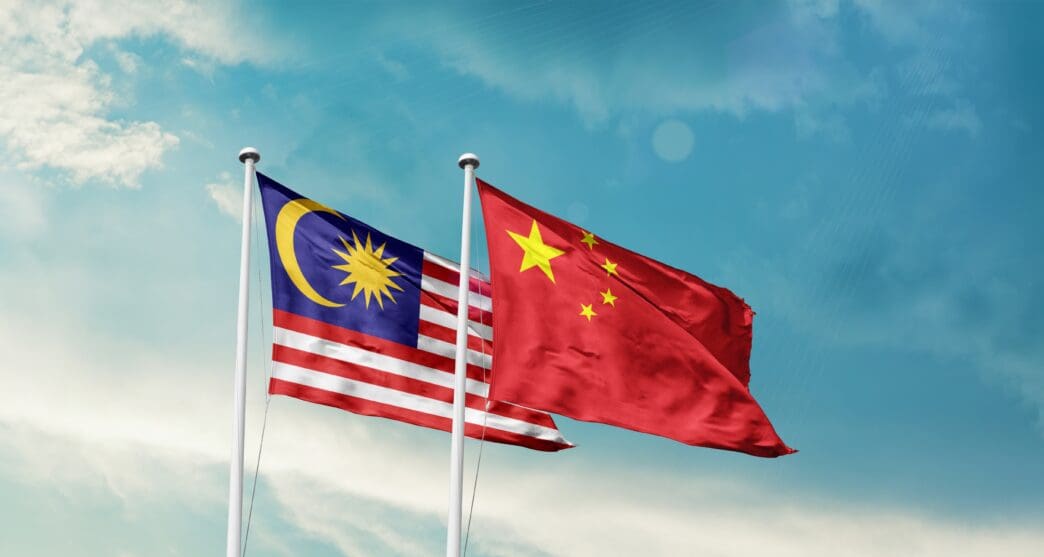 The national flags of Malaysia and China waving side-by-side against a blue sky.