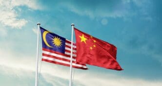 The national flags of Malaysia and China waving side-by-side against a blue sky.