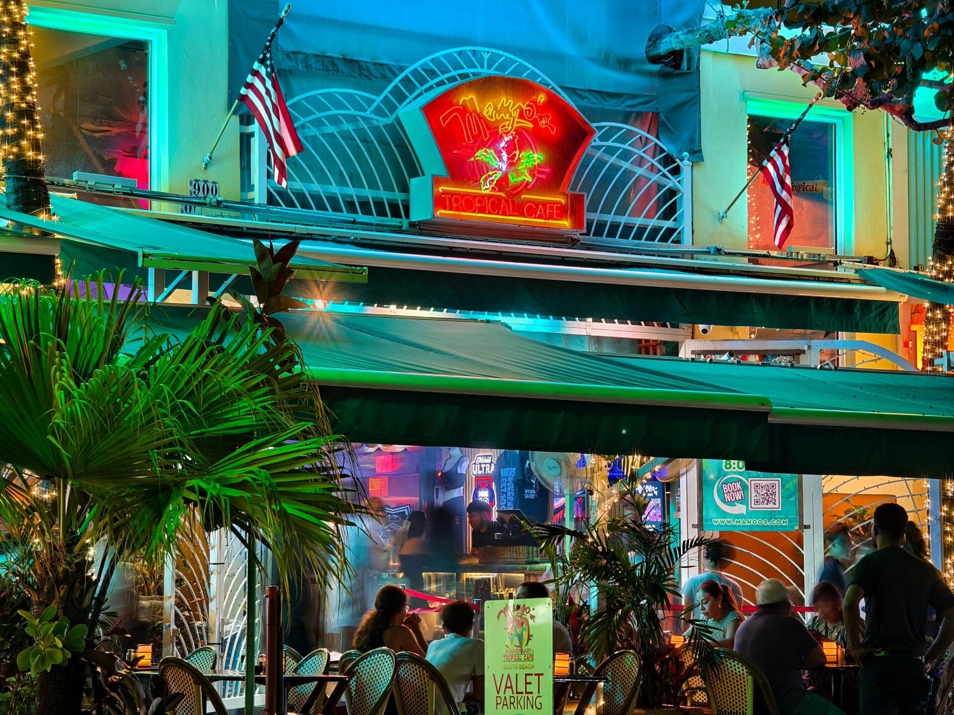 The vibrant neon sign of Mango's Tropical Cafe in South Beach glows above patrons at its outdoor patio at night.
