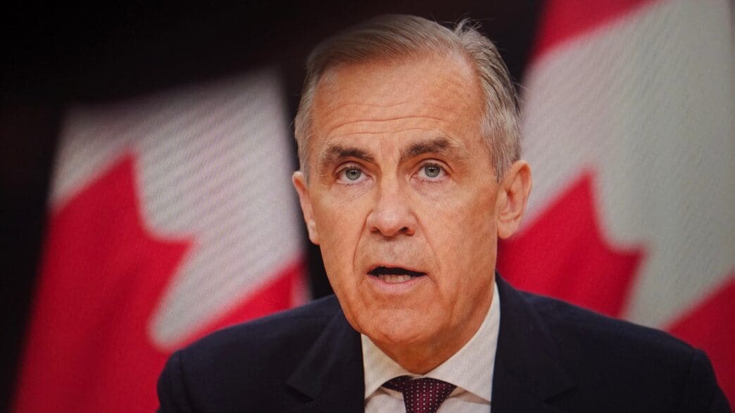 Close-up of Mark Carney speaking publicly, backed by two blurred, prominent Canadian flags on a screen
