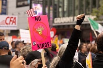 A protester holds a pink "NO KINGS!" sign with a US flag at a crowded May Day political rally in Los Angeles.