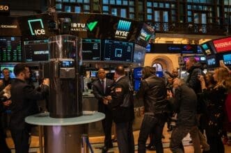 New York Mayor Eric Adams speaking with a trader at the central podium of the NYSE floor, surrounded by media and screens.