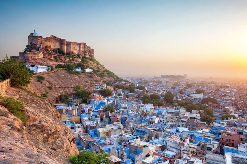 Panoramic view of the massive Mehrangarh Fort towering over the densely packed blue buildings of Jodhpur, India, at sunrise.