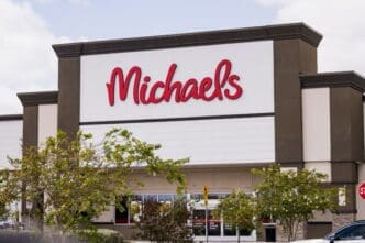 Exterior view of a Michaels craft store building featuring its logo in red script letters on a white and brown facade.