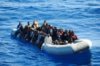 Overloaded grey rubber dinghy crowded with numerous African migrants navigating the deep blue waters of the Mediterranean Sea.