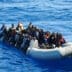Overloaded grey rubber dinghy crowded with numerous African migrants navigating the deep blue waters of the Mediterranean Sea.
