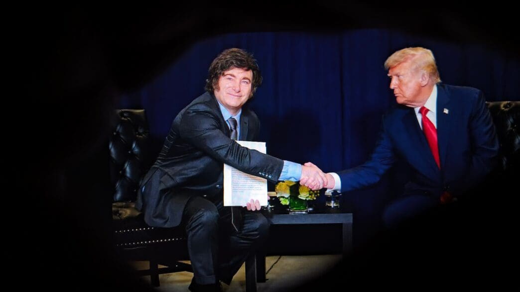 Argentine President Javier Milei and President Donald Trump shake hands across a small table while sitting on stage at a conservative political conference.