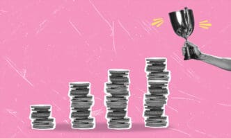 Four stacks of coins in ascending order with a hand holding a trophy over the last one.