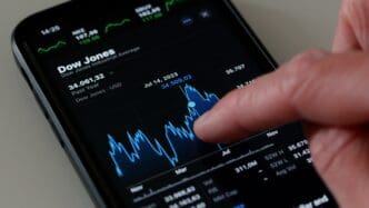 A finger touches the Dow Jones Industrial Average chart on an iPhone stock app.