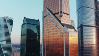 The modern skyscrapers of the Moscow City business center, including the bronze Mercury City Tower, glow in the sunset.