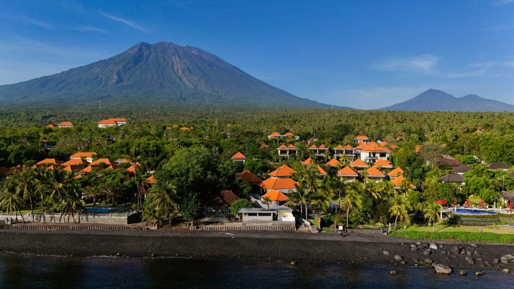 A scenic view of a coastal village in Bali with Mount Agung, the island's highest volcano, rising in the background.