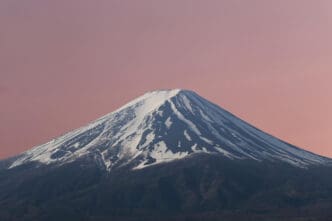 A close-up of the snow-capped peak of Mount Fuji against a pink sky.