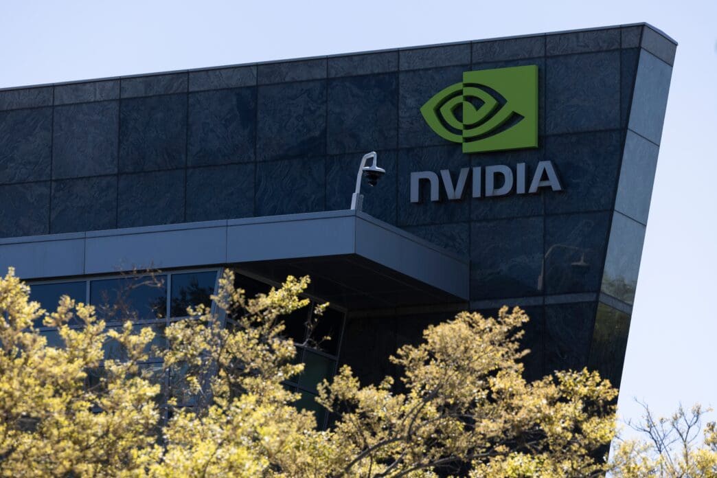 Close-up of the green NVIDIA corporate logo and name on the dark, angular, stone-tiled facade of its headquarters building