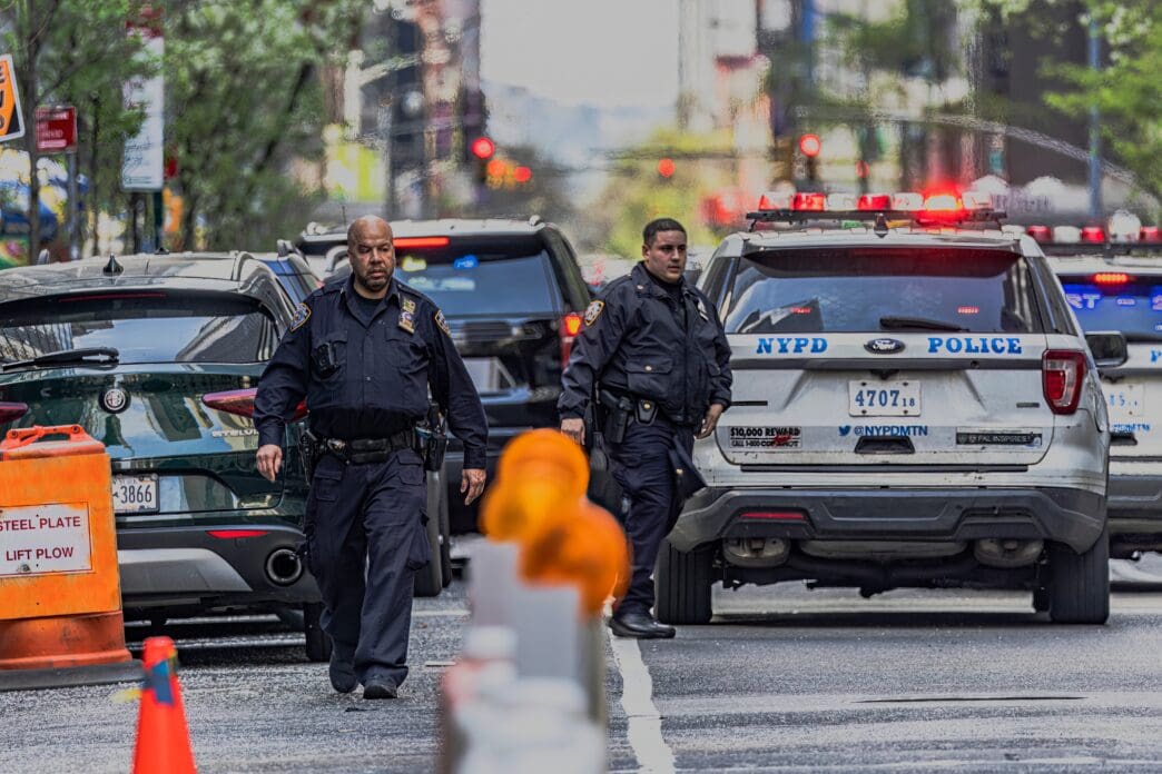 NYPD officers in uniform and police vehicles on a city street, suggesting an active scene