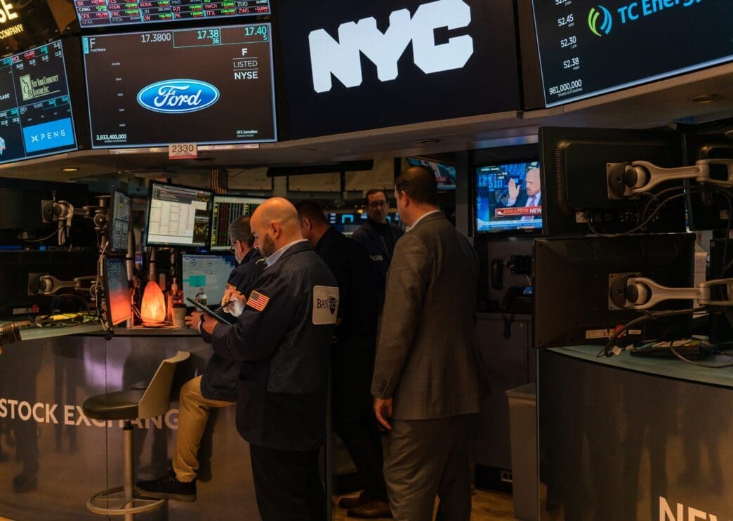 Traders and executives standing on the NYSE floor, dominated by screens showing stock prices and the Ford Motor Company logo