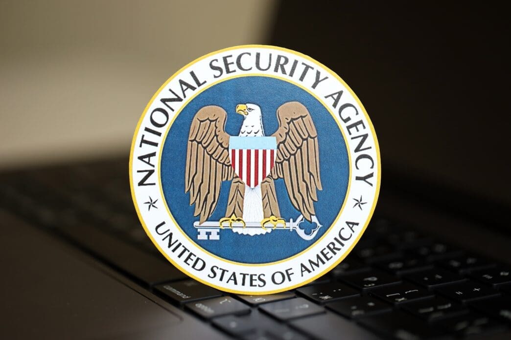 A circular sticker with the National Security Agency (NSA) seal rests on a dark laptop keyboard, showing the eagle and key emblem.