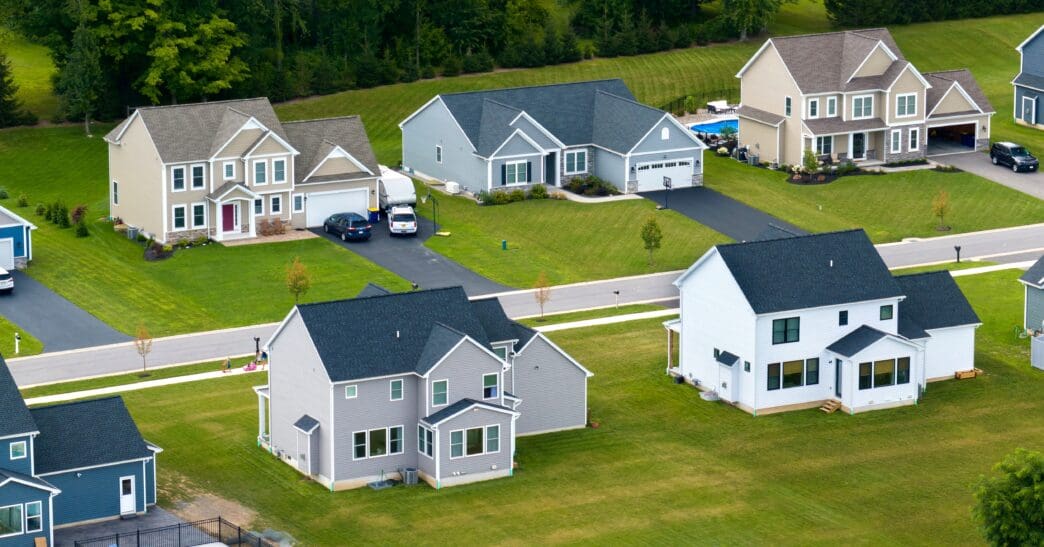 Aerial view of large, modern, single-family homes with green lawns in a suburban development.