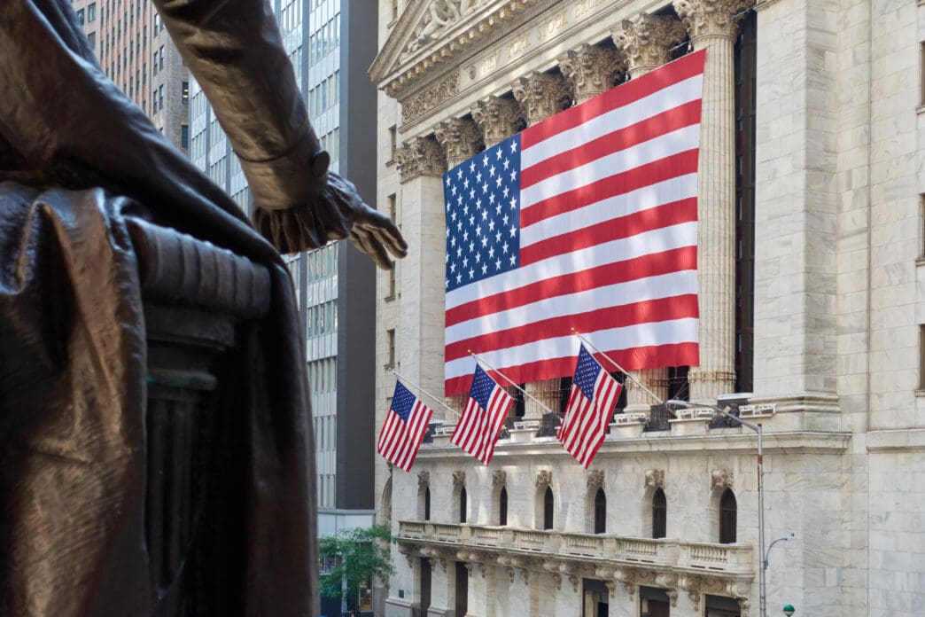 The NYSE building, draped with a large US flag, viewed from behind the George Washington statue.