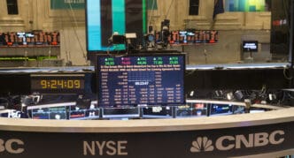 Monitors displaying stock quotes and ticker information hang over the NYSE trading floor.