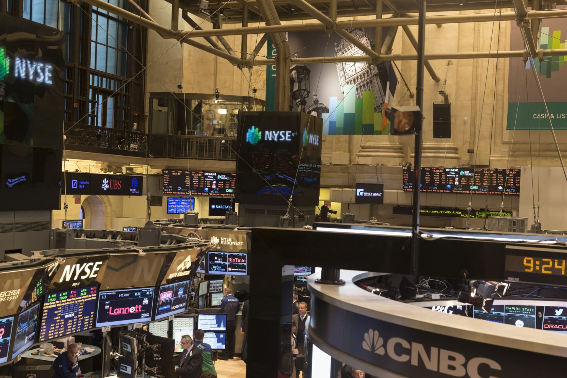 Wide interior view of the complex, multi-level New York Stock Exchange trading floor covered with screens and structural beams.