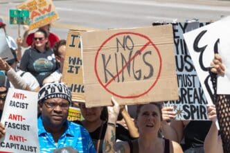 A woman holds a "No Kings" sign high during a political protest in Atlanta, surrounded by other demonstrators with signs.