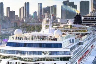 Passengers stand on the upper deck of the Norwegian Jade cruise ship, with smoke rising from its funnel against the Miami skyline.