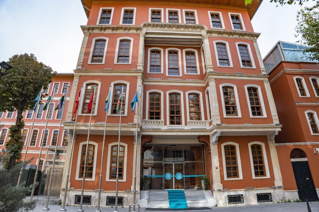 The red-brick headquarters building of the Organization of Turkic States in Istanbul, with flags flying at the entrance.