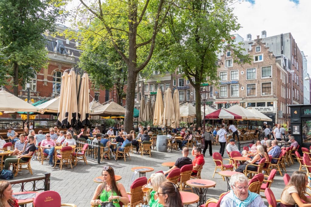 People enjoy outdoor dining and drinks at packed cafe terraces on the bustling Leidseplein square in Amsterdam.