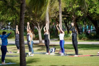 A group of women doing yoga stretches on mats in a park in Miami Beach, FL.