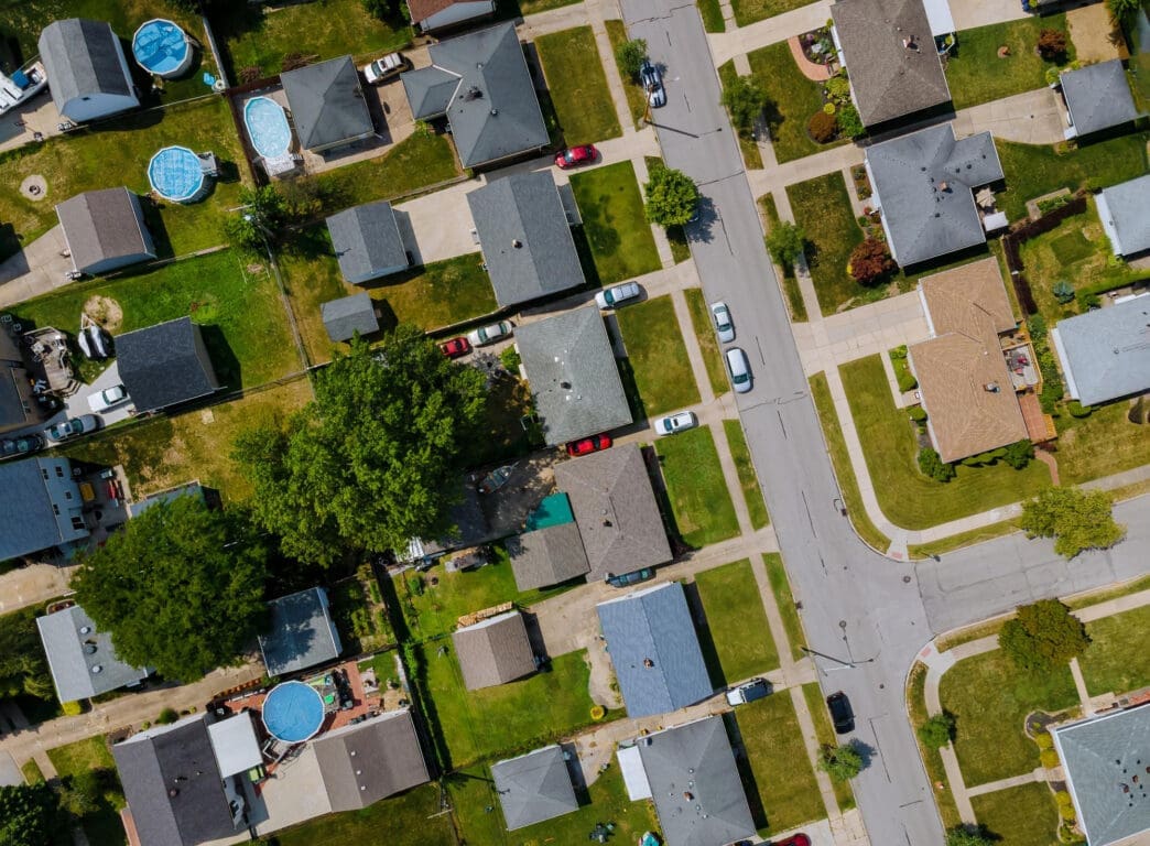 High aerial view of a dense, grid-patterned suburban neighborhood with single-family houses and green lawns.