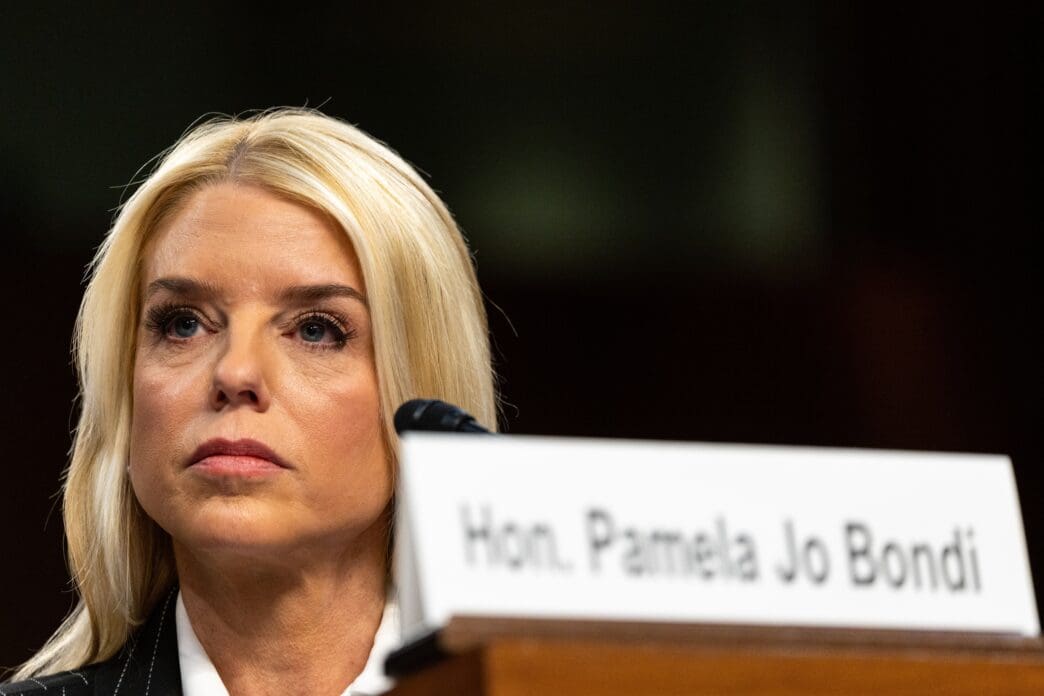 Close-up of Pamela Bondi, a blonde woman, listening intently during a hearing, with her nameplate visible