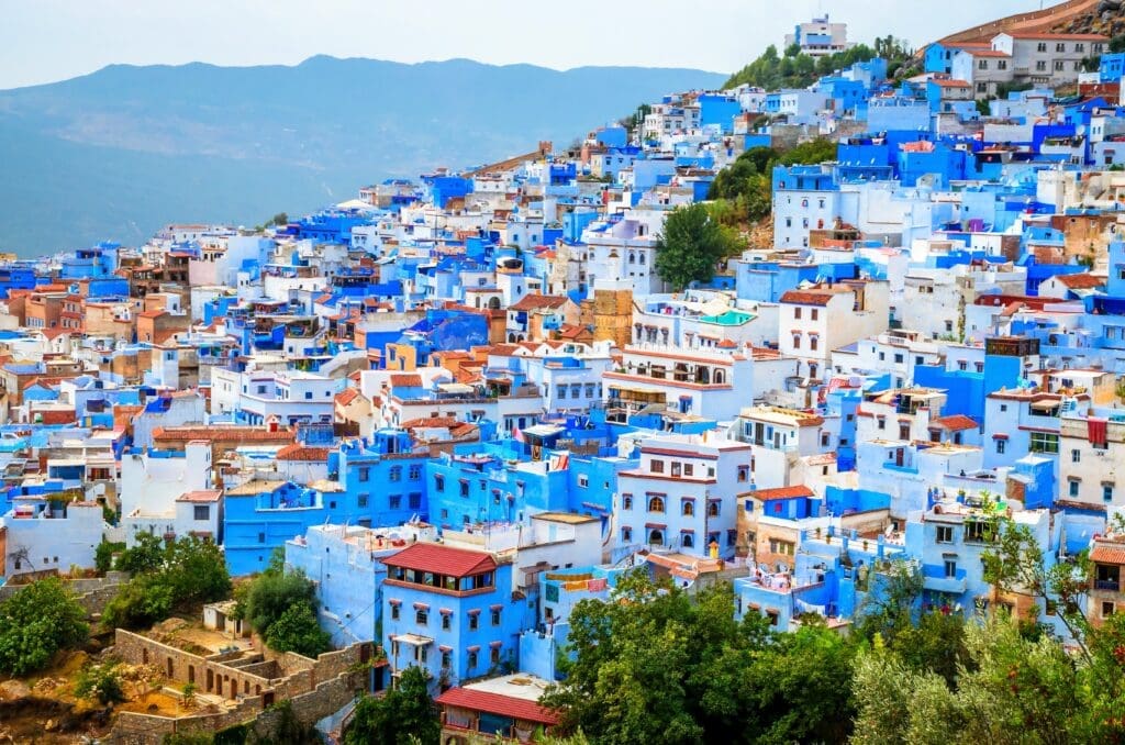 Panoramic view of the dense, cascading blue and white buildings of Chefchaouen's medina covering a steep hillside in Morocco.