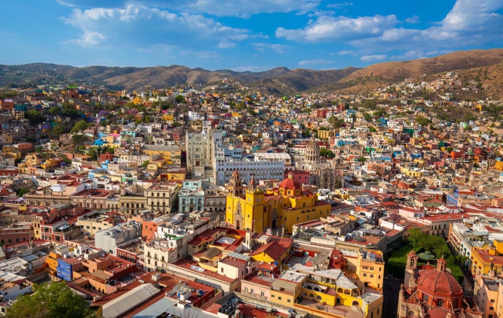 Panoramic view of the colorful, dense city of Guanajuato, Mexico, nestled in a valley among dry, rolling hills.