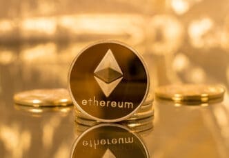 A physical Ethereum coin standing on a stack, reflected on a golden surface.