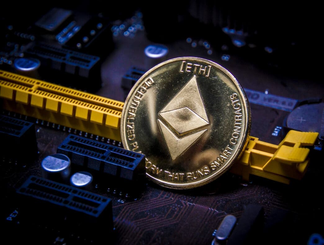 A physical gold Ethereum (ETH) coin resting on a dark computer motherboard.