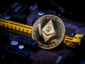 A physical gold Ethereum (ETH) coin resting on a dark computer motherboard.