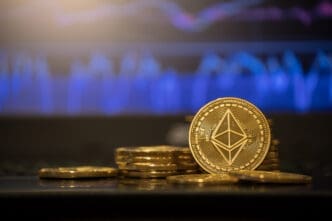 Physical gold Ethereum coins are stacked on a surface with a glowing blue financial chart blurred in the background.