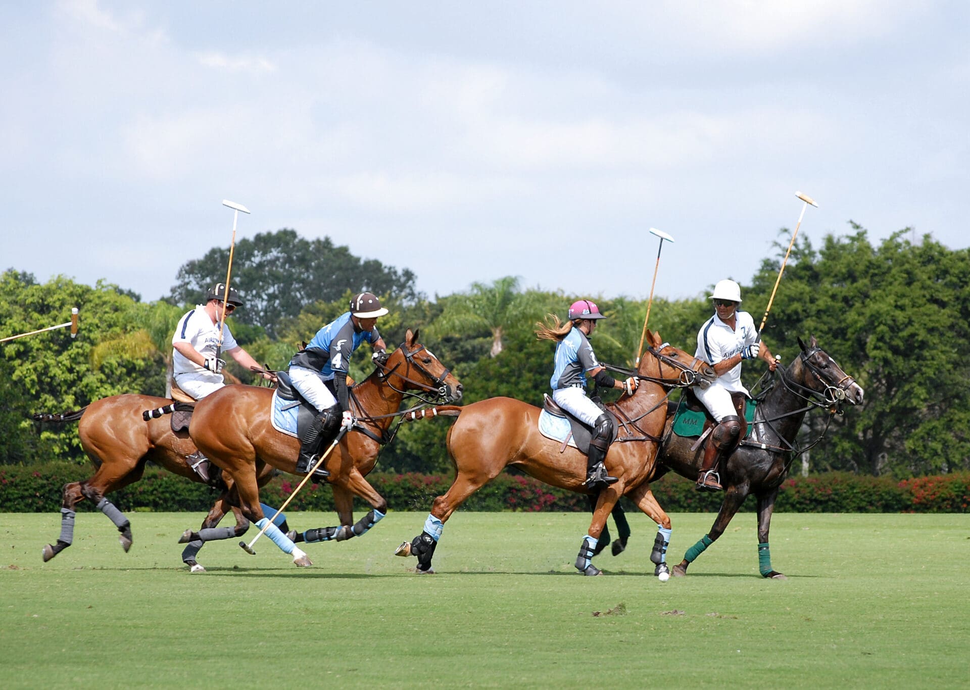 Four polo players on galloping horses chasing the ball across a vibrant green field during a fast-paced match.