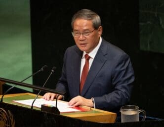 Chinese Premier Li Qiang wearing a navy suit and red tie speaks at a podium during the UN General Assembly session.