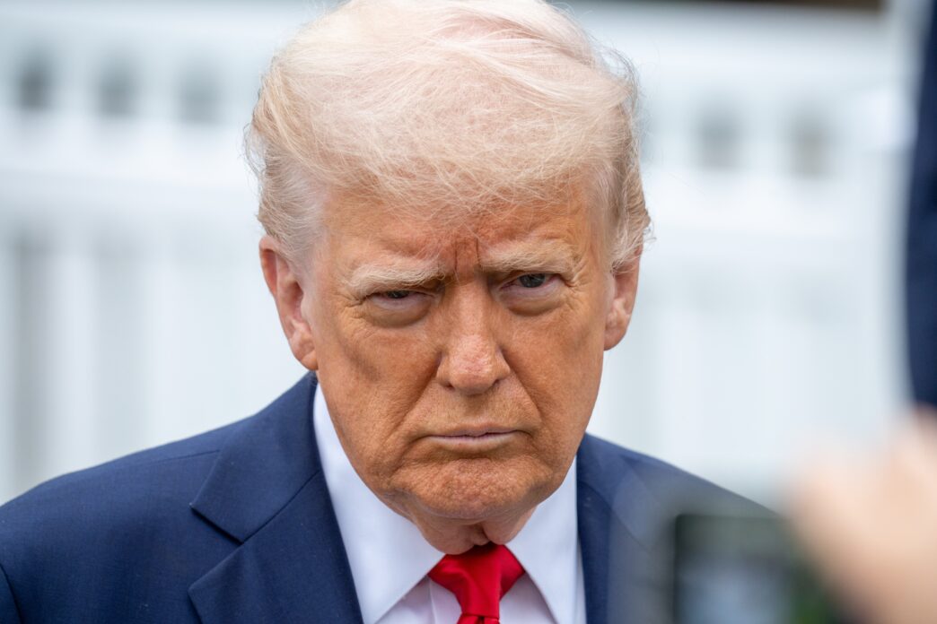 A close-up of President Donald Trump in a suit and red tie looking at the press.