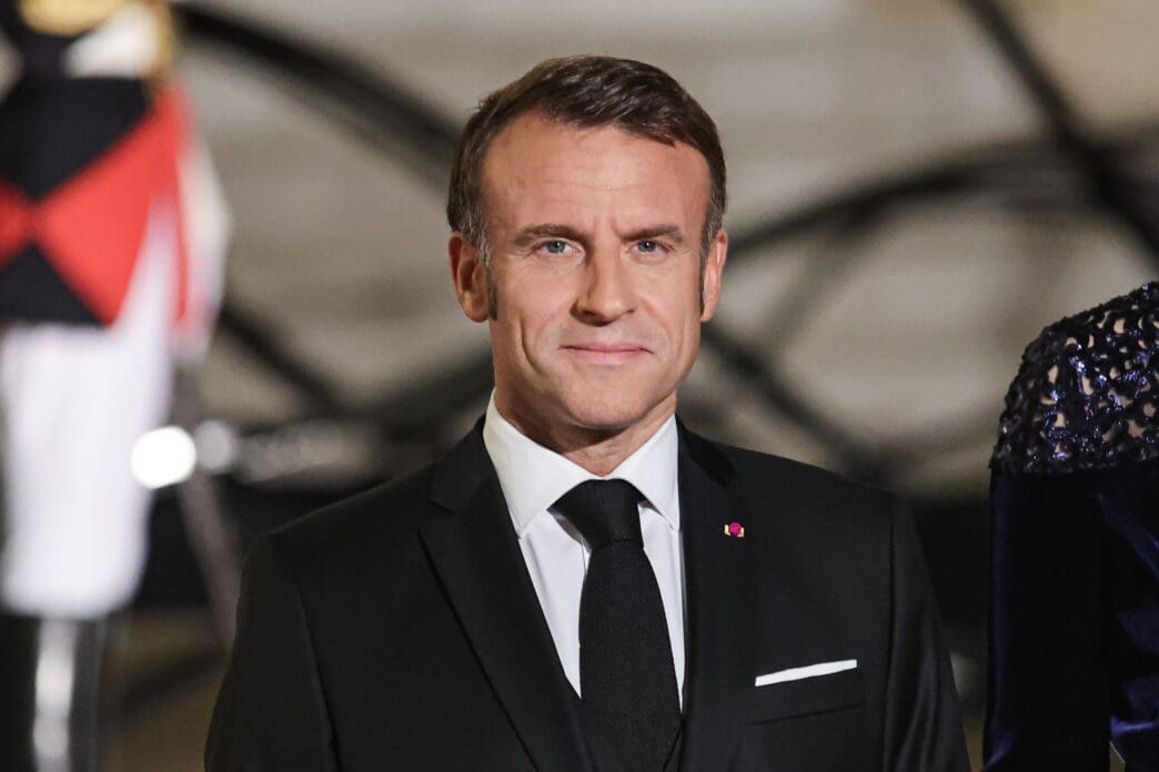 President Emmanuel Macron in a black suit with a white shirt and black tie.