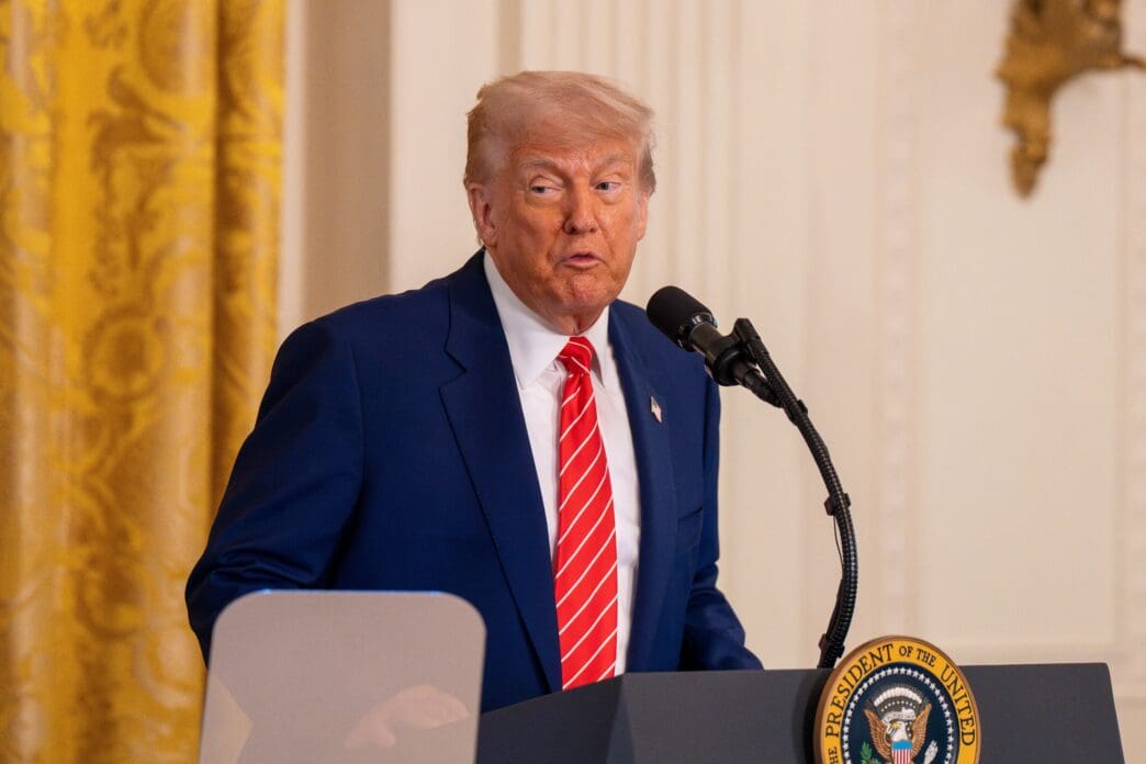 President Donald Trump speaking at a podium with the Presidential Seal in the East Room of the White House.