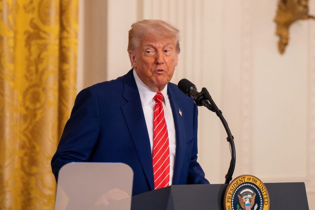 President Donald Trump speaking at a podium with the Presidential Seal in the East Room of the White House.