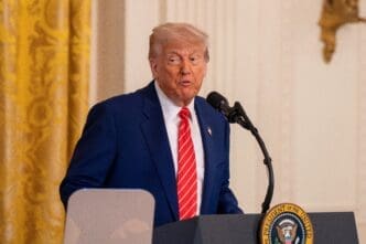 President Donald Trump speaking at a podium with the Presidential Seal in the East Room of the White House.