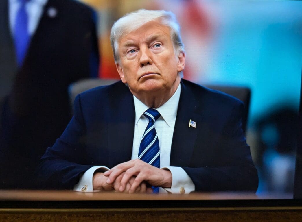President Donald Trump sits at a table in the Roosevelt Room with his hands clasped, looking upward during a meeting.